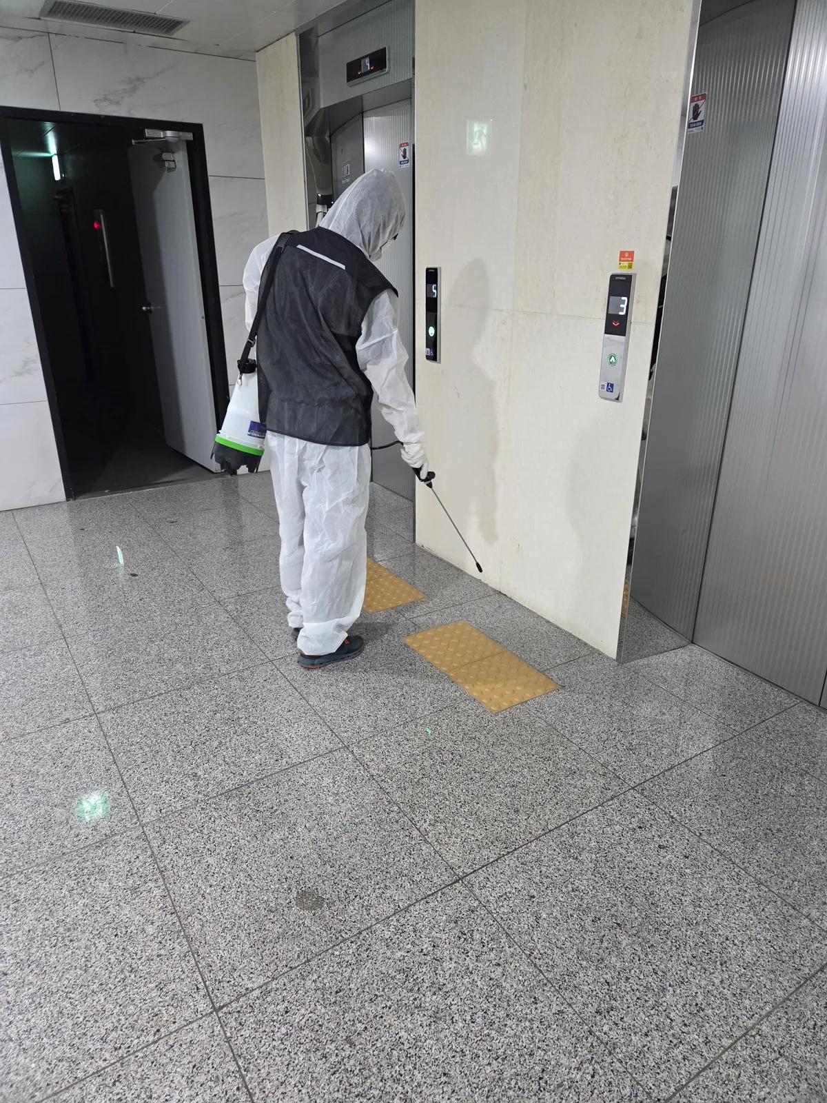 승강기 앞에서 분사구를 바닥 쪽으로 향하고 작업하는 모습