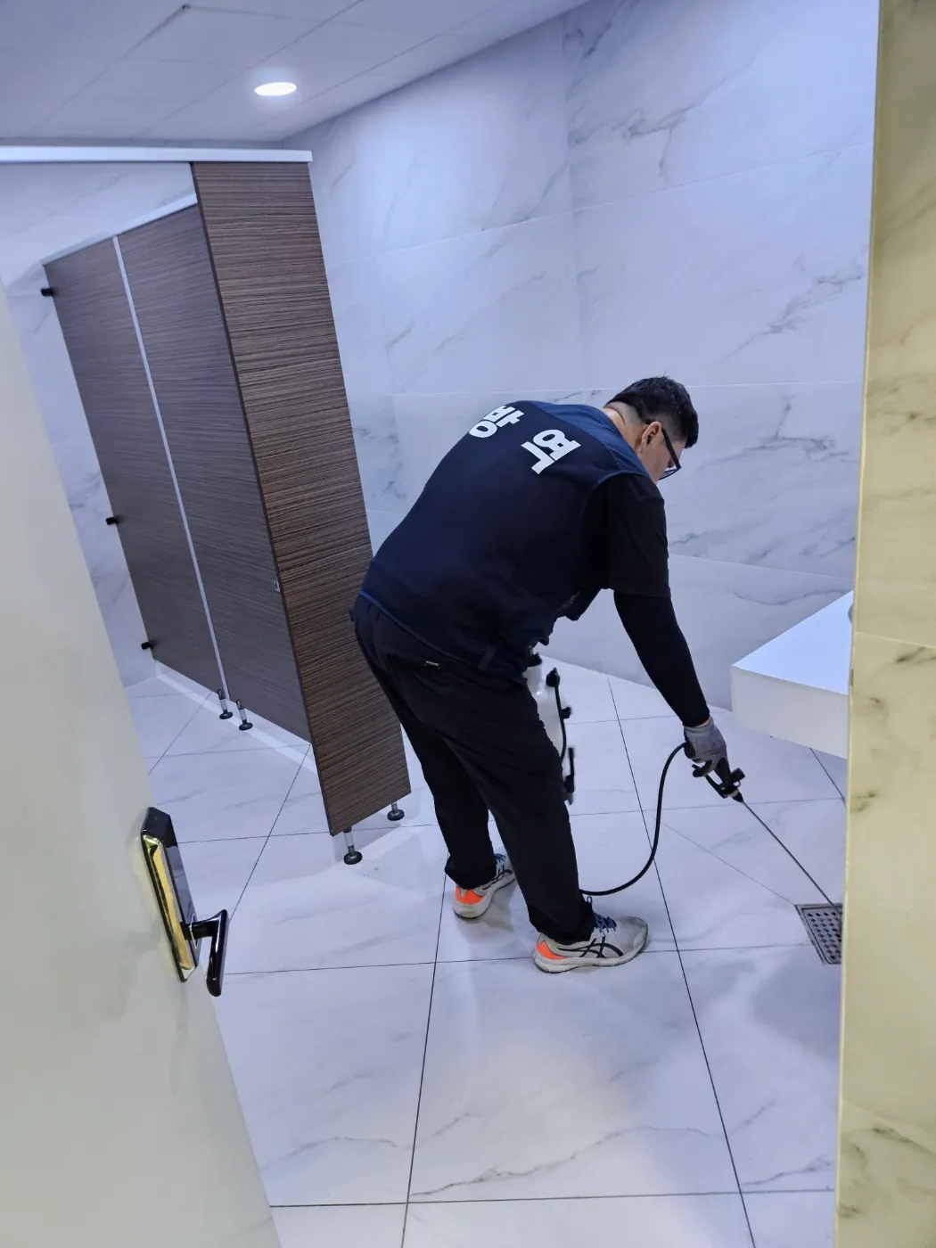 공용 화장실 배수구 주변에 방역 약제를 적용하는 작업자